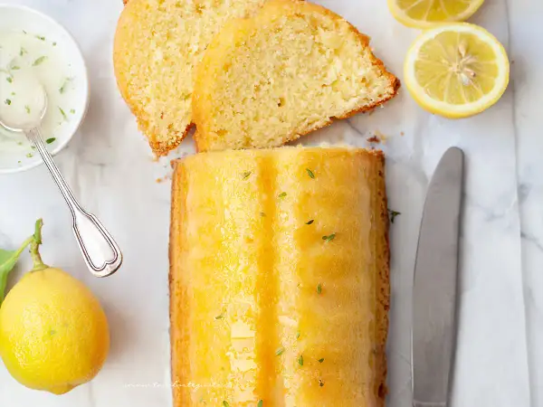 Un delizioso plumcake al limone glassato, con fette affettate, limoni freschi, una ciotolina di glassa e un coltello.