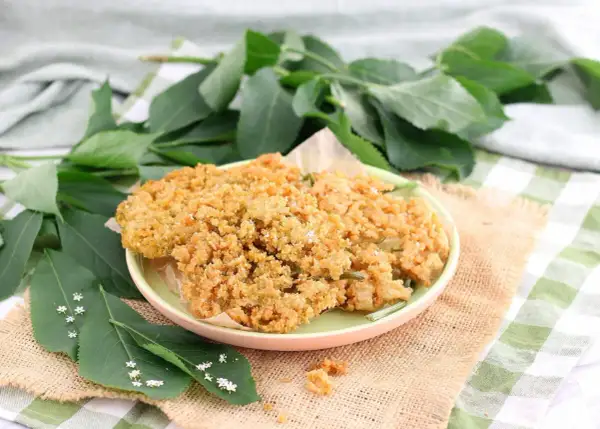 Fiori di sambuco fritti dorati e croccanti su un piatto, con foglie verdi e piccoli fiori di sambuco tutt'intorno.