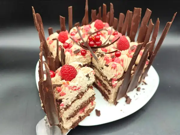 Una golosa torta cioccolato e lamponi, decorata con panna, frutti rossi e scaglie di cioccolato. Una fetta è già stata servita.